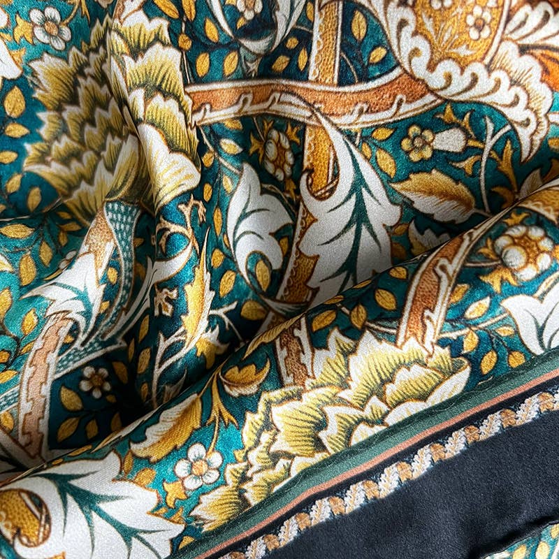 Eine Nahaufnahme des Koustrupco Seidenschal Morris Windrush grün (50 x 50 cm) mit detaillierten Blumen- und Blattmustern in Grün, Gold, Weiß und Braun und einer dekorativen Bordüre am Rand.