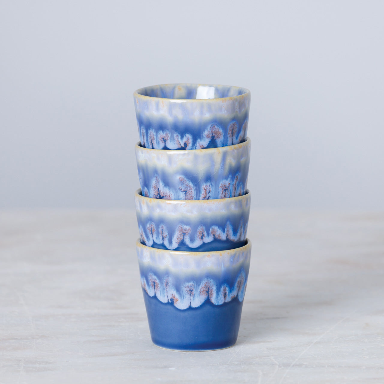 Vier Costa Nova 'Grespresso' Espressotassen Denim Blau aus Steingut und Keramik (9 cl) mit gewelltem, blauem Muster sind aufeinander gestapelt und stehen vor einem schlichten, hellen Hintergrund.