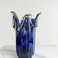 Die „Murano Dream Große Giusy“-Vase aus blauem, originalem Murano-Glas (H 32, Ø 20 cm) mit wellenförmigen, klar akzentuierten Kanten und glänzender Oberfläche steht auf einer weißen Marmorplatte – ein handgefertigtes Glaskunstwerk aus Italien.