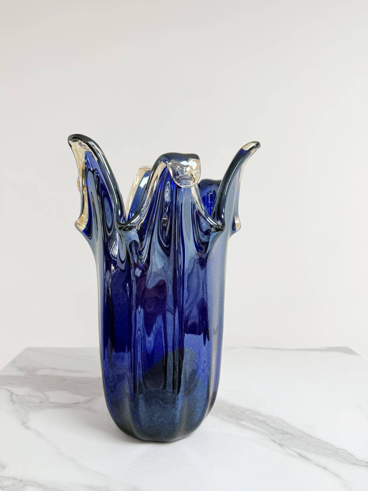 Die „Murano Dream Große Giusy“-Vase aus blauem, originalem Murano-Glas (H 32, Ø 20 cm) mit wellenförmigen, klar akzentuierten Kanten und glänzender Oberfläche steht auf einer weißen Marmorplatte – ein handgefertigtes Glaskunstwerk aus Italien.