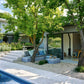 Ein modernes Gästehaus am Pool mit Glasschiebetüren wird von Bäumen beschattet. In der Nähe bietet ein gepolsterter Sitzplatz auf Kies eine perfekte Terrassengestaltung, inspiriert von "Die schönsten Terrassen und Sitzplätze" aus dem Callwey Verlag. Eine Treppe führt in das darüber liegende Haupthaus.