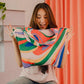 Eine Person mit langen braunen Haaren lächelt aufgeregt, während sie eine Notabag | Shopping Tote 'Flow' von Notabag, eine bunte wiederverwendbare Einkaufstasche, vor einem orangefarbenen Vorhang hält.