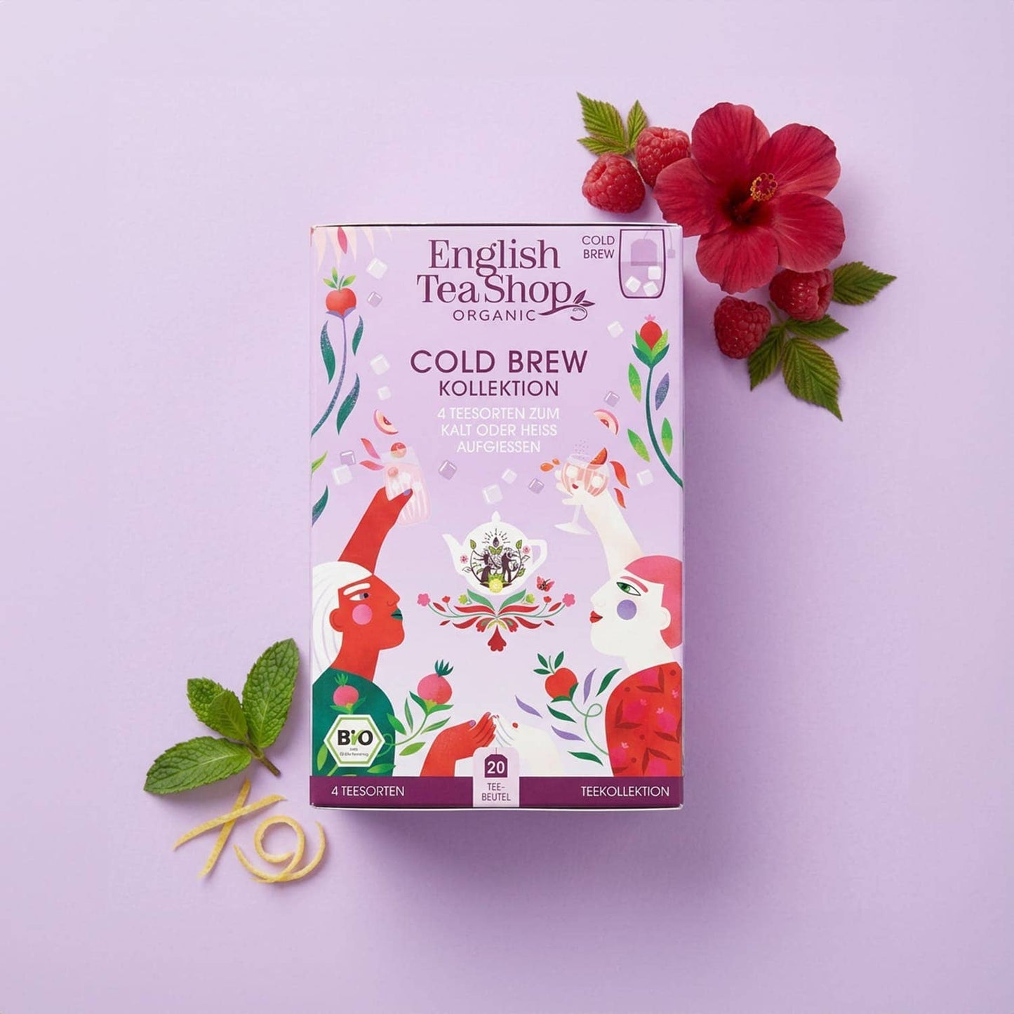 Eine Schachtel English Tea Shop | 'Cold Brew' Bio-Tee Kollektion 4 Sorten, 20 Teebeutel, steht auf einem pastelllila Hintergrund mit Minzblättern, Himbeeren und Hibiskus. Das Bio-Erfrischungsgetränk ist zuckerfrei und zeigt bunte Illustrationen von Teetrinkern.