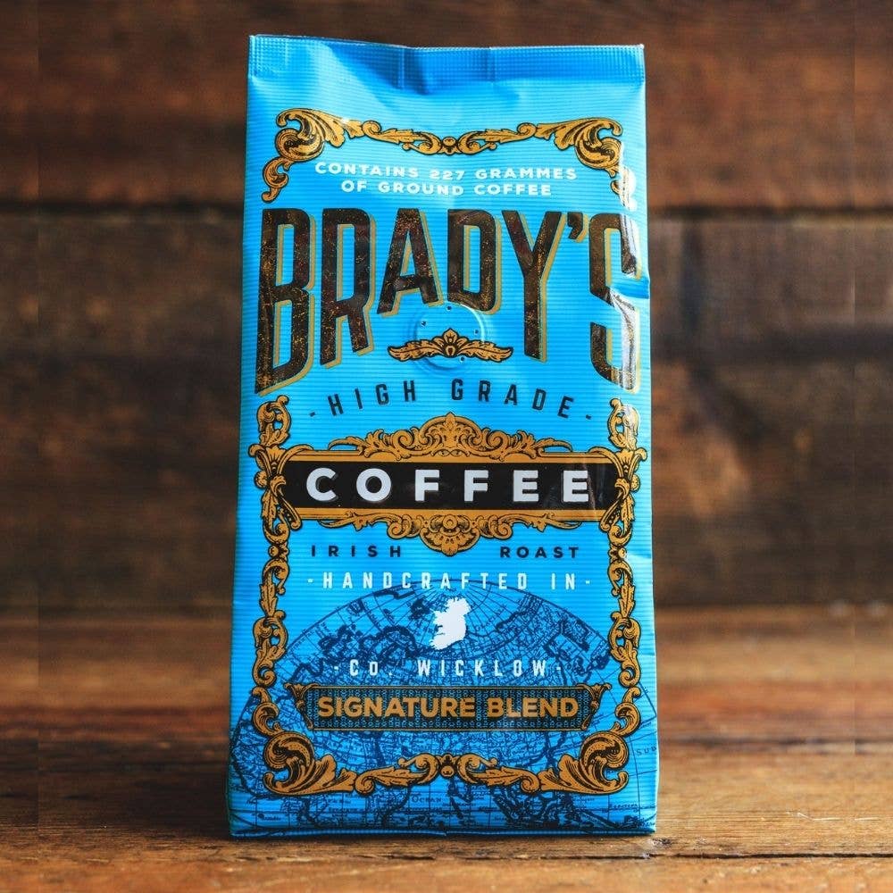 Eine blaue Tüte Brady's Coffee Company | 227 g gemahlener Signature Blend Kaffee mit goldenen und schwarzen Verzierungen und der Aufschrift "handcrafted high-grade Irish Roast from Co. Wicklow, steht auf einer Holzunterlage.
