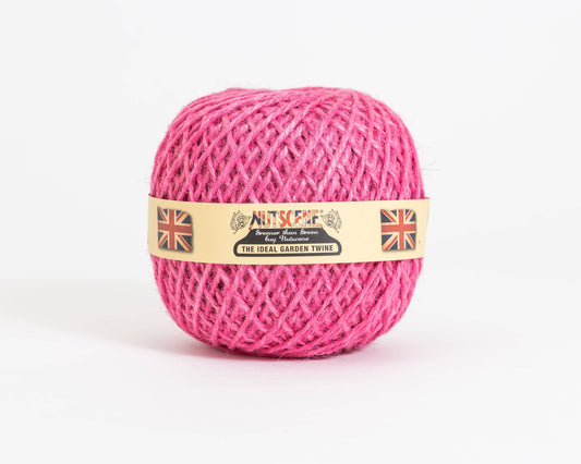 Auf einem schlichten weißen Hintergrund liegt ein Knäuel leuchtend pinkfarbenes „Nutscene | Heritage Jutegarn in Pink“ (130 m) von Nutscene Twines Ltd. Auf dem beigen Etikett ist der Name „Nutscene“ zu sehen, flankiert von zwei Union-Jack-Flaggen, eine auf jeder Seite.