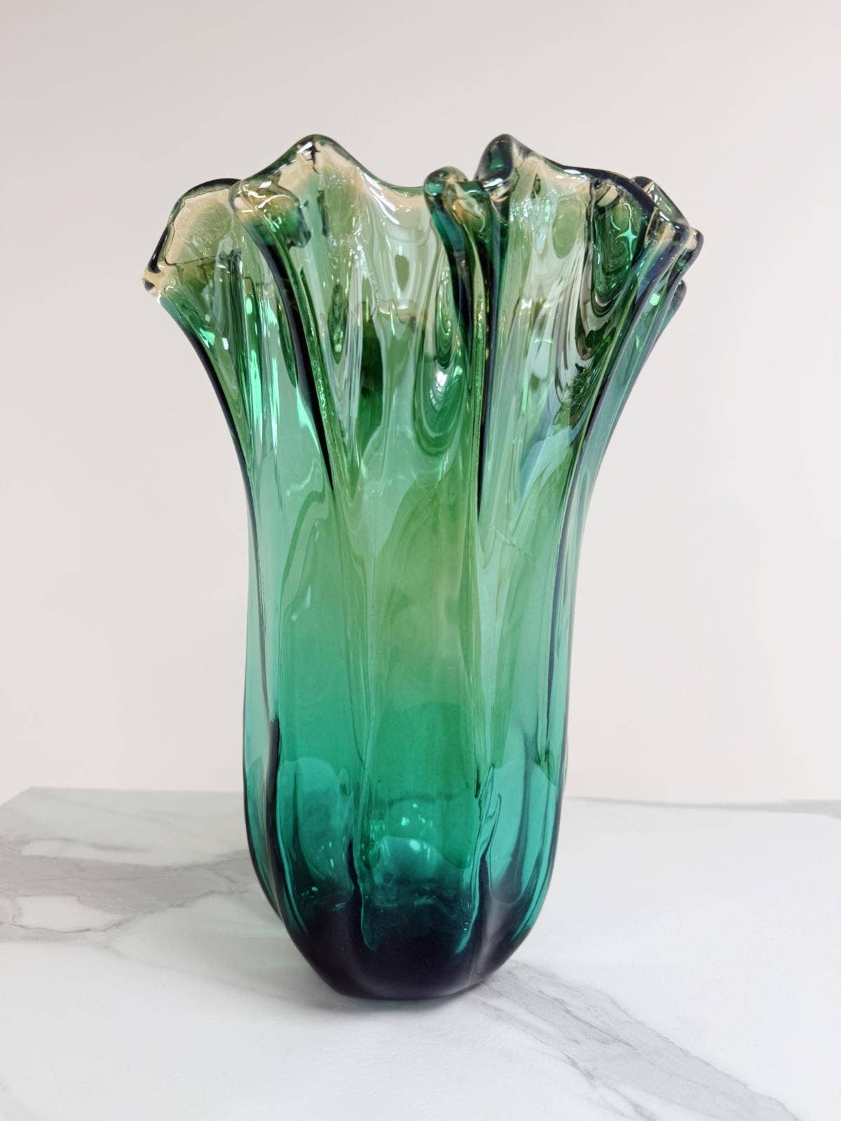 Die Murano Dream „Fazzoletto“-Vase aus grünem Murano-Glas (H 32 Ø 24 cm) besticht durch ihre hohe, wellenförmige Form und den sanften Farbverlauf von Grün zu Transparent – handgefertigt und stilvoll vor hellgrauem Hintergrund präsentiert.