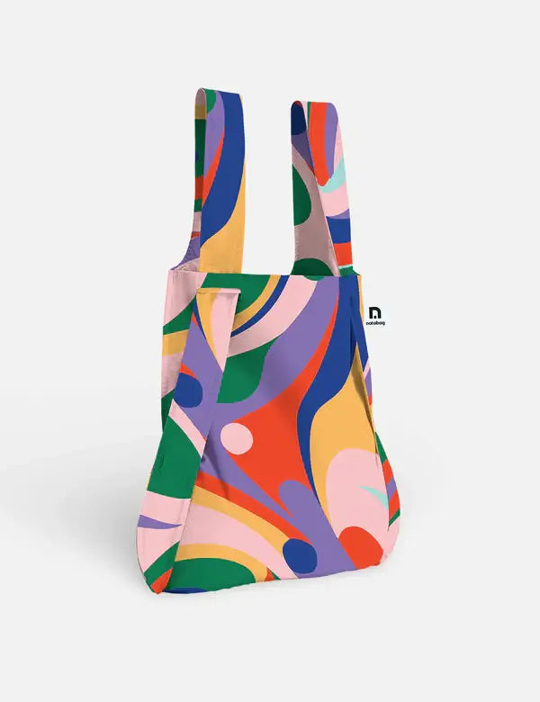 Die Notabag | 'Flow' Kombination aus Tasche & Rucksack verfügt über breite Griffe und ein lebendiges abstraktes Wirbelmuster in Rot, Blau, Grün, Pink, Gelb und Lila auf Weiß - die ideale umweltfreundliche Tasche für den täglichen Gebrauch.