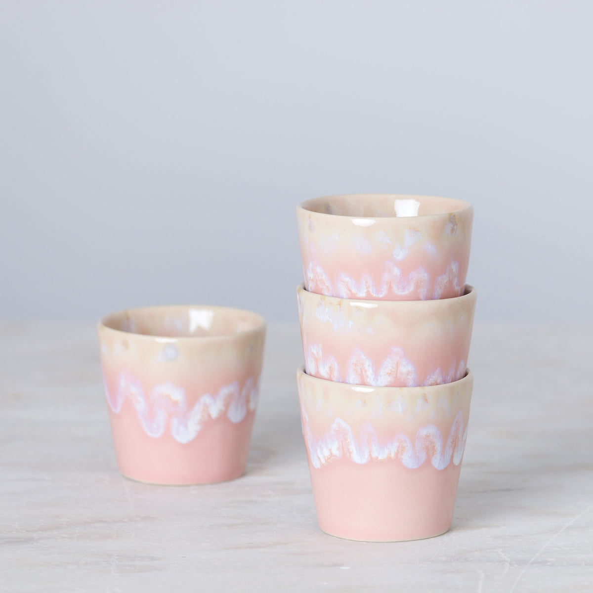 Vier pastellrosa „Grespresso“-Espressotassen von Costa Nova aus Steingut und Keramik (9 cl) sind so angeordnet, dass drei Tassen übereinandergestapelt sind und eine daneben auf einer hellen Unterlage vor einem blassen Hintergrund steht. Dieses Set in verschiedenen Farben verleiht jedem Kaffeemoment einen mediterranen Touch.