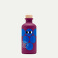 Eine violette Flasche mit einem Holzkorken, blauen Kreisen, zwei Cartoon-Augen und dem Etikett "Yiayia and friends | Gereifter Balsamico-Essig 200 ml," zehn Jahre gereift, Product of Greece by yiayia and friends.
