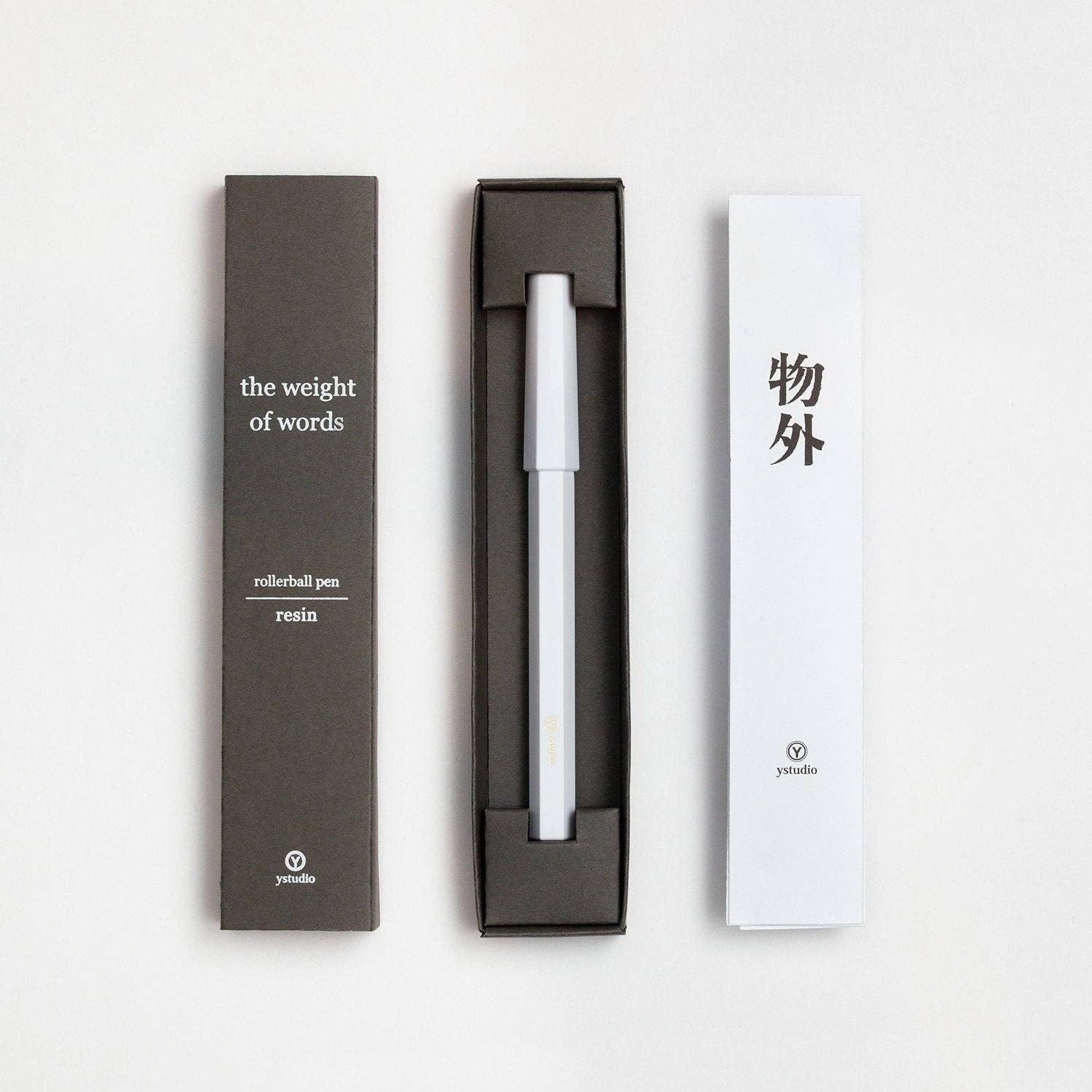 Der YSTUDIO | Harz-Rollerball-Stift (Schwarz) von ENTREPÔT, ein hochwertiges Schreibgerät in einer eleganten Verpackung mit dem Schriftzug "the weight of words", präsentiert sich in einer schwarzen Schachtel mit weißem Einsatz mit chinesischen Schriftzeichen und ystudio-Branding.