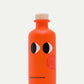 Eine leuchtend orangefarbene Flasche mit einem Holzdeckel, zwei auffälligen Augengrafiken und "yiayia and friends®" auf der Vorderseite. Ein griechischer Stempel an der Seite hebt sie als Yiayia and friends Natives Olivenöl extra mit Chili hervor.