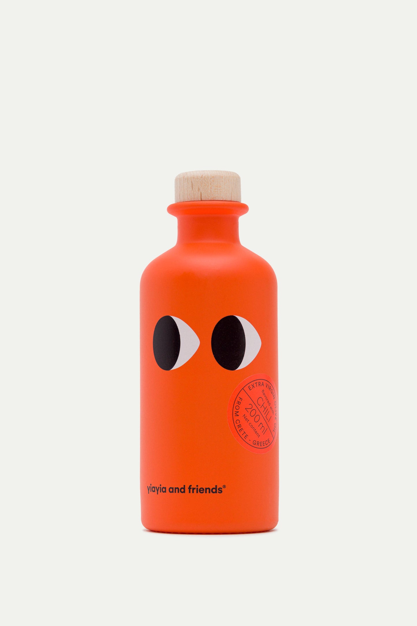 Eine leuchtend orangefarbene Flasche mit einem Holzdeckel, zwei auffälligen Augengrafiken und "yiayia and friends®" auf der Vorderseite. Ein griechischer Stempel an der Seite hebt sie als Yiayia and friends Natives Olivenöl extra mit Chili hervor.