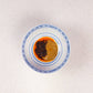 In einer blau-weißen Schüssel befinden sich ein Klecks „White Mausu Ltd White Mausu | Black Bean Rayu Sauce“ – eine braune Paste aus fermentierten Bohnen – und ein Löffel voll scharfer Soße mit Chiliflocken; die Schüssel steht auf einer hell gesprenkelten Arbeitsplatte.
