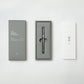 Der YSTUDIO | Klassischer Revolve Kugelschreiber Slim (Glänzendes Silber) von ENTREPÔT liegt elegant in einer grauen THE WEIGHT OF WORDS-Box samt Anleitung mit asiatischen Zeichen - alles stilvoll auf weißem Grund präsentiert.