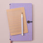 Das Tinne Mia Notizbuch A6 'Nougat Grid' mit FSC-Papier und beige gepunktetem Raster liegt samt weißem Stift auf einem lavendelfarbenen Notizbuch mit Knopfverschluss auf zartrosafarbenem Untergrund.