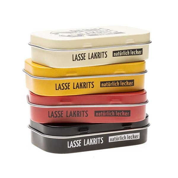 Ein gestaffelter Stapel von vier LASSE LAKRITS-Dosen, darunter die gelbe "Dose Reines Lakritz Waldfrucht", weist das charakteristische LASSE LAKRITS-Branding und die Geschmacksrichtungen Reines Lakritz, zuckerfreies Lakritz und Lakritz Waldfrucht auf.