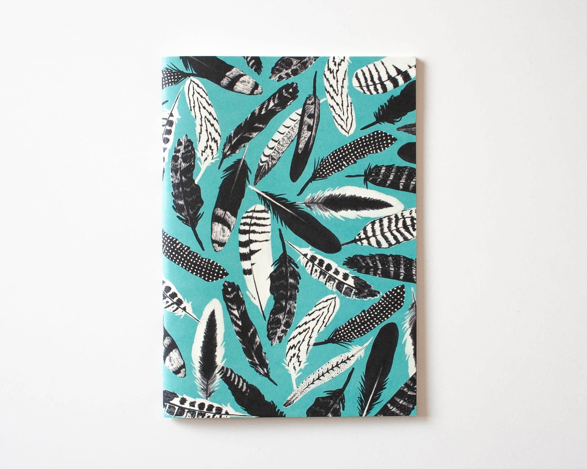 Das Papaya Paper Products Notizheft A5 mit blauem Federmuster liegt geschlossen auf weißer Fläche; das Munken Print Cream Papier garantiert ein angenehmes Schreiberlebnis.
