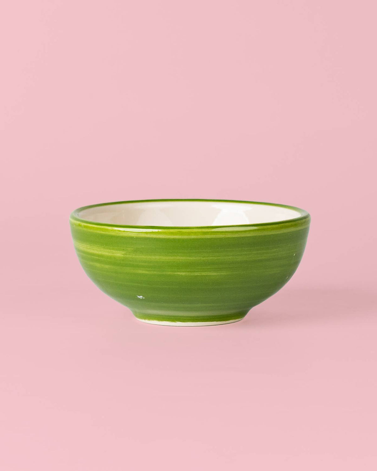 Eine kleine grüne Mini-Keramikschale „Olive“ von Alfar Tierra Cocida mit weißer Innenseite steht auf einem rosa Hintergrund und unterstreicht den Charme der mediterranen Keramik, die in Spanien von Alfar Tierra Cocida handgefertigt wird.