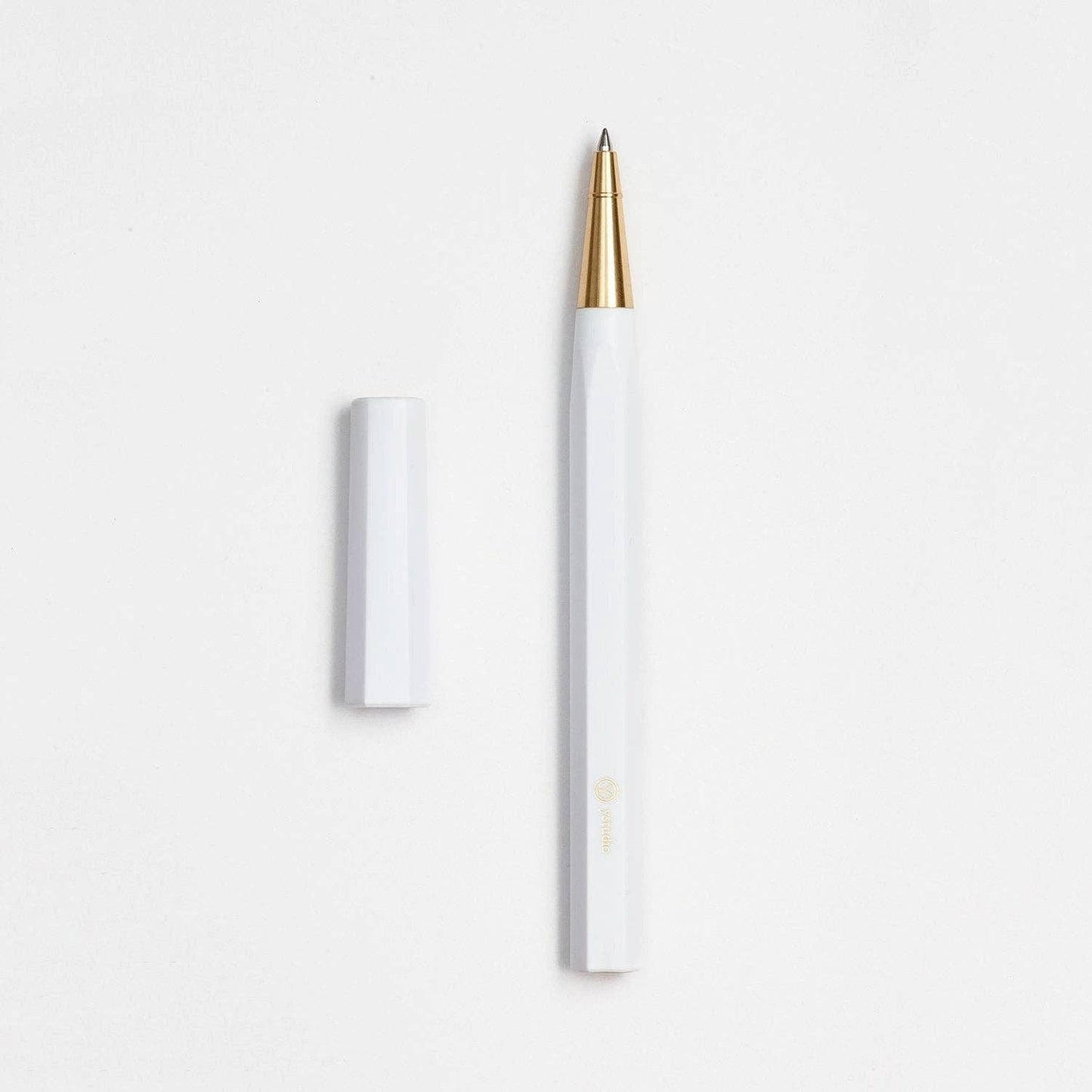 Der ENTREPÔT YSTUDIO | Harz-Rollerball-Stift (Weiß), mit Acryl- und Messingkörper sowie goldener Spitze, liegt auf einer weißen Fläche neben der passenden Kappe.