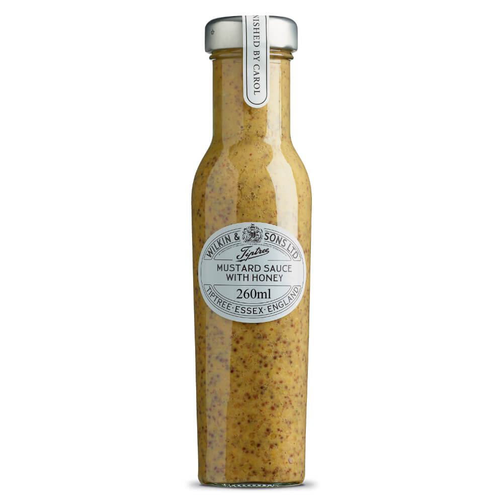 Eine hohe Glasflasche mit „Wilkin & Sons Tiptree Honig-Senf-Sauce“, 260 ml, mit silbernem Verschluss und einem Etikett mit schwarzer Beschriftung. Diese cremig-gelbe Senfsauce enthält sichtbare Senfkörner und spiegelt die charakteristische Qualität von Wilkin & Sons wider.