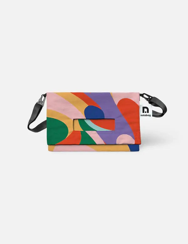 Die Notabag | 'Flow' Leichte Umhängetasche von Notabag ist eine farbenfrohe Umhängetasche mit einem abstrakten Muster in grün, pink, lila, rot, gelb und blau. Sie verfügt über einen schwarzen verstellbaren Gurt, einen Henkelausschnitt auf der Klappe und ein sichtbares Notabag Logo-Tag.