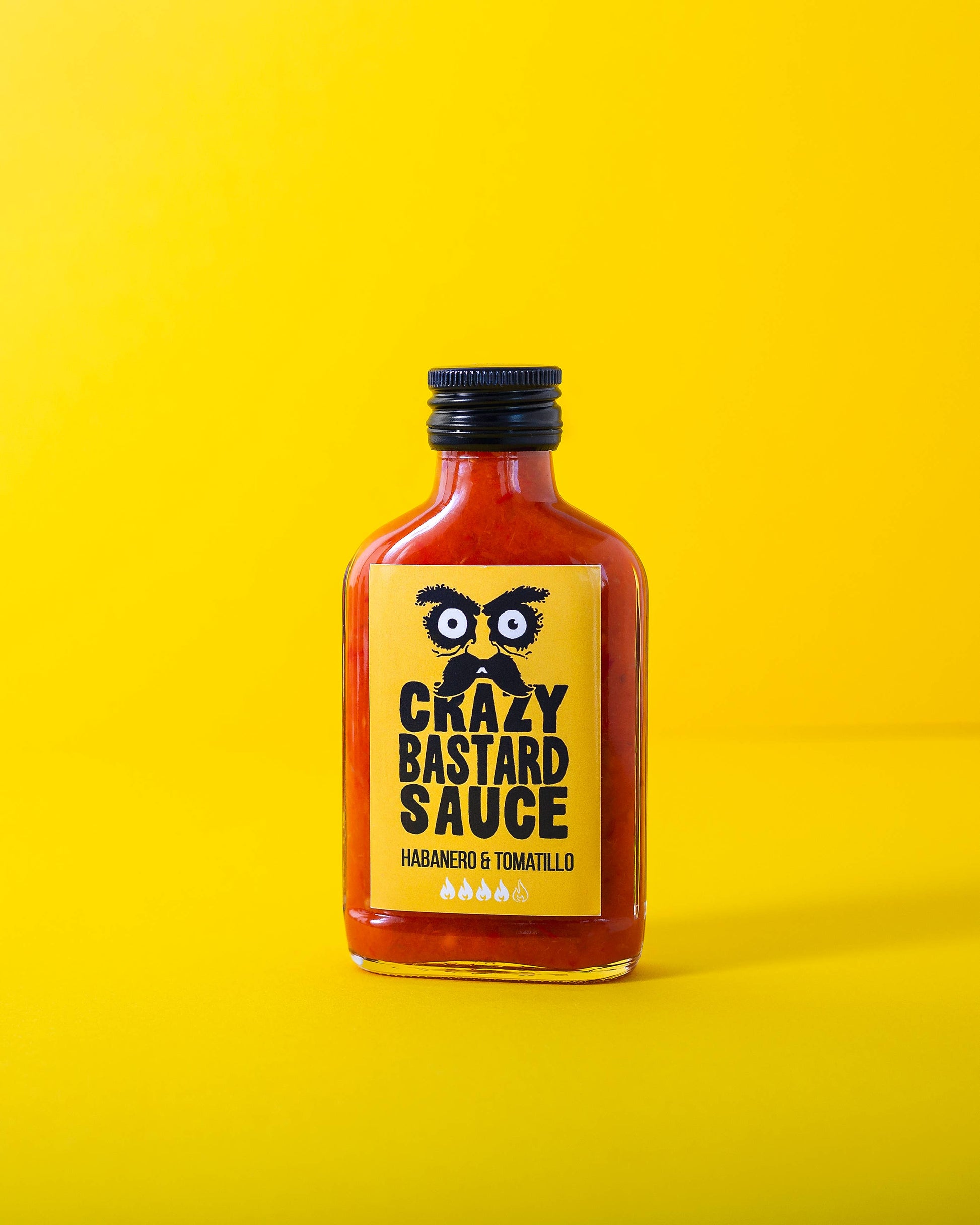 Eine 100-ml-Flasche Crazy Bastard Sauce Habanero & Tomatillo scharfe Soße, mit gelbem Etikett, fettgedruckter schwarzer Schrift und illustrierten Augen auf gelbem Hintergrund - ideal für Fans von scharfen Soßen.