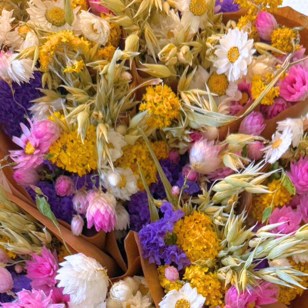 Eine Nahaufnahme von „Wildflowers by Floriette“ | Trockenblumenstrauß „Dutch“, ca. 50 cm, mit gelben, rosa, violetten und weißen Trockenblumen, kunstvoll kombiniert mit beigen Gräsern und in braunes Papier eingewickelt – ein wunderschönes Arrangement von „Wildflowers by Floriette“, das natürliche Eleganz verkörpert.