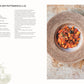 Ein Teller mit Nudeln mit Tomatensoße, Oliven und Kräutern steht auf einem strukturierten Teller. Auf der linken Seite ist ein Puttanesca-Rezept aus dem DK Verlag "Vegetarisch | Meisterwerk der vegetarischen Küche" abgebildet, darunter Tomaten.