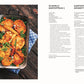 Eine Auflaufform mit goldgelb gebratenen Kartoffelscheiben und Möhren aus "Vegetarisch | Meisterwerk der vegetarischen Küche" vom DK Verlag steht auf einem blauen Handtuch. In der Nähe liegen gekochte grüne Erbsen auf einer weißen Tischplatte verstreut.