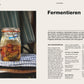 Ein Glas mit buntem fermentiertem Gemüse steht auf einem gestreiften Tuch. Daneben liegt das Buch "Selbstversorgung aus dem Garten | Mehr als nur ein Trend" aus dem DK Verlag, aufgeschlagen auf einer Seite mit deutschen Fermentationsrezepten und Tipps.