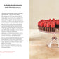 Eine Schokoladentorte mit Himbeeren steht auf einem rosafarbenen Tortenständer, eine Scheibe davor hebt vegane und glutenfreie Rezepte aus dem Buch "Kleine Kuchen | 50 Rezepte für Mini-Kuchen, kleine Torten & mehr" des DK Verlags vor einem hellrosa Hintergrund hervor.