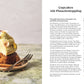 Ein aufgeschnittener Cupcake mit grüner Pistazienglasur und Nüssen liegt auf einem Teller mit einer Gabel. Daneben steht "Kleine Kuchen | 50 Rezepte für Mini-Kuchen, kleine Torten & mehr" vom DK Verlag. Der Hintergrund ist sanft verschwommen.