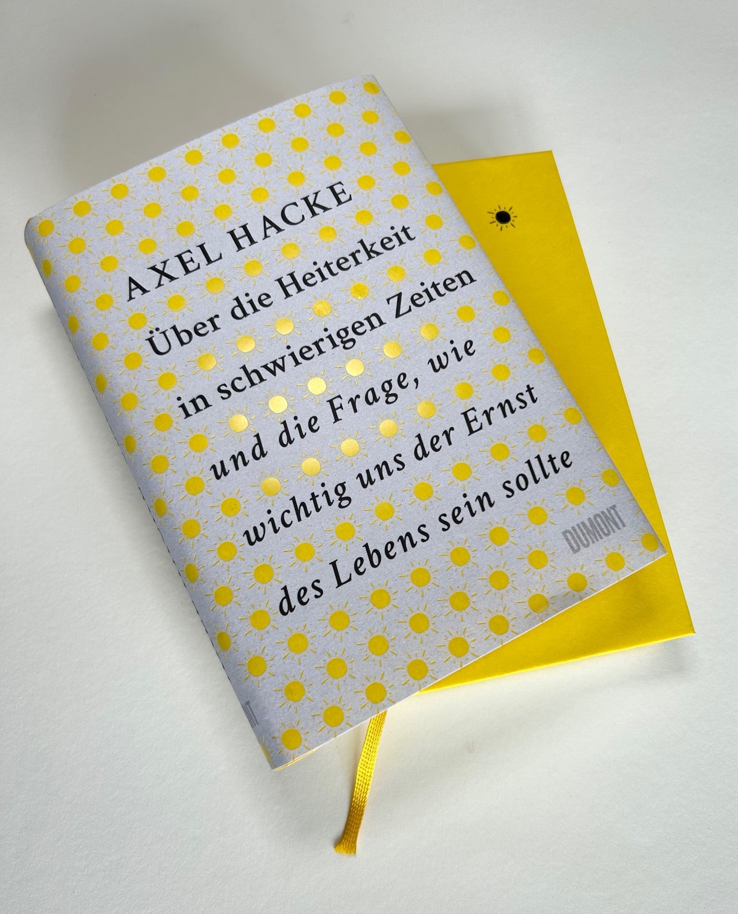 Das deutsche Buch "Über die Heiterkeit | Unterhaltsam, klug und persönlich" aus dem Dumont Verlag zeigt ein sonnengemustertes Cover auf leuchtend gelbem Hintergrund, inspiriert von Friedrich Schillers Konzept der Heiterkeit.