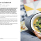 Eine Person hält eine Schüssel Miso-Suppe mit Tofu und grünen Zwiebeln mit Stäbchen in der Hand. Im Hintergrund sind eine gemusterte Fläche und ein aufgeschlagenes Buch LEON | Hundert Suppen aus dem Dumont Verlag mit deutschen Suppenrezepten zu sehen.