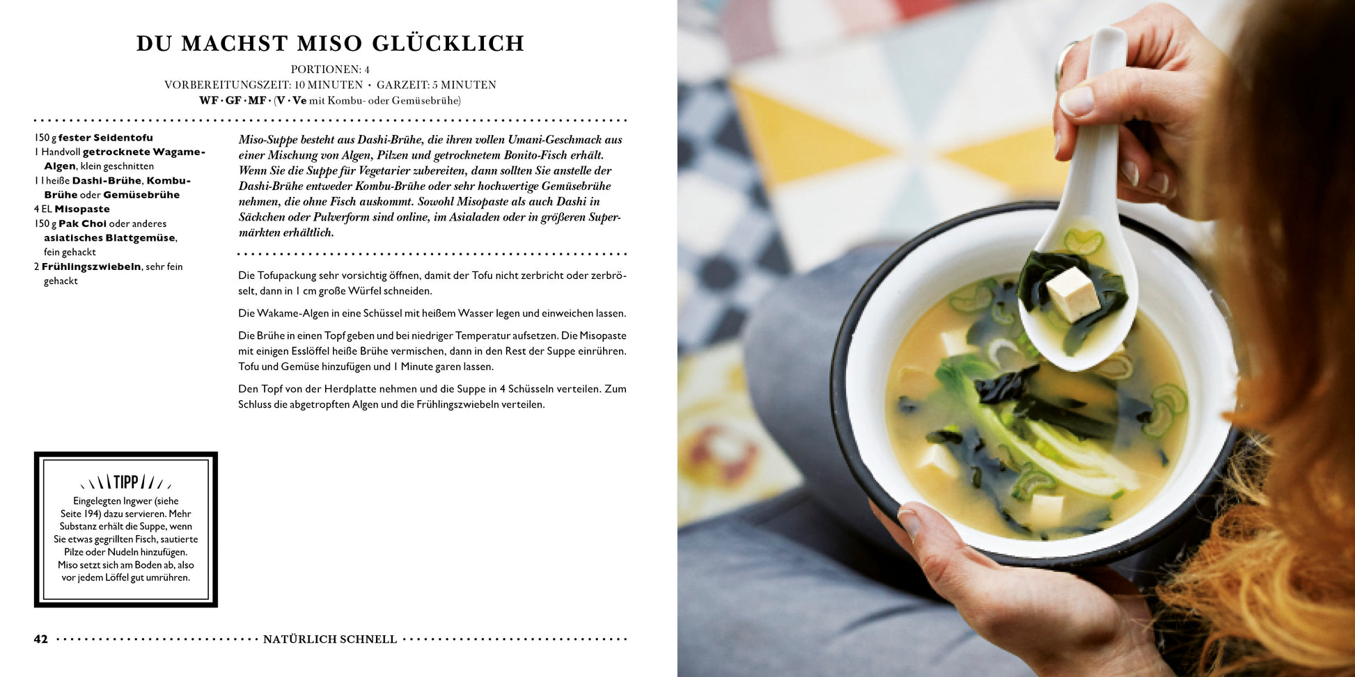 Eine Person hält eine Schüssel Miso-Suppe mit Tofu und grünen Zwiebeln mit Stäbchen in der Hand. Im Hintergrund sind eine gemusterte Fläche und ein aufgeschlagenes Buch LEON | Hundert Suppen aus dem Dumont Verlag mit deutschen Suppenrezepten zu sehen.