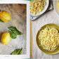 Ein aufgeschlagenes Kochbuch, "Die Küche von Amalfi | 75 authentische Rezepte" vom Gerstenberg Verlag, zeigt frische Zitronen und Teller mit Spaghetti - einige mit Zitrone - die den Glanz der italienischen Küche von der Amalfiküste einfangen.