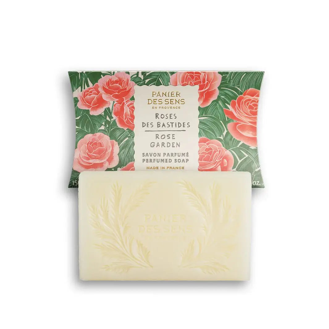 Ein Riegel Panier Des Sens | Duftseife Rose des Bastides 150 g mit geprägtem Blattmotiv liegt vor der blumigen Verpackung mit der Aufschrift "Rose Garden" und "Made in France" - authentische französische feste Seife von Panier Des Sens.