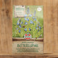 Eine 600 g-Packung Sperli's | Bitterlupine Bodenkur Saatgut steht auf einer Holzfläche mit blauen Lupinenblüten und Grünzeug. Der deutsche Text hebt die Wirksamkeit des Saatguts zur Bodenverbesserung hervor. Marke: Sperli's.