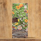Eine farbenfrohe Saatgutpackung mit der Aufschrift Sperli's | Naschvielfalt Blumenmischung für Falter & Nützlinge zeigt blühende Wildblumen und Pflanzensymbole mit dem Markenzeichen von Sperli's auf einem Holzhintergrund.