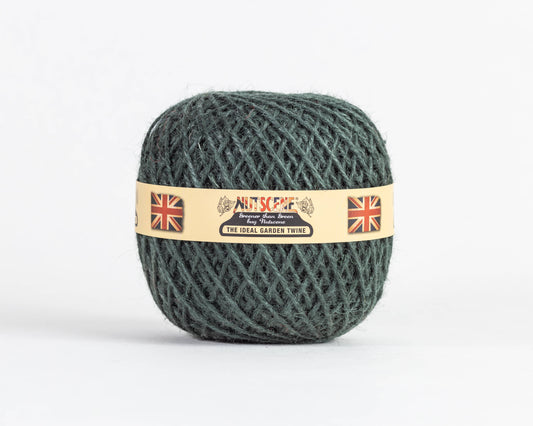 Ein Knäuel dunkelgrünes „Heritage Jutegarn“ von Nutscene Twines Ltd | Botanical, 130 m, umwickelt mit einem beigen Etikett, auf dem zwei britische Flaggen sowie die Aufschriften „Nutscene“ und „The Ideal Garden Twine“ vor einem schlichten weißen Hintergrund abgebildet sind.
