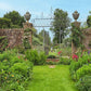 Inspiriert von Gärtnern wie Gott in England aus dem Callwey Verlag: ein üppig grüner Garten mit bunten Blumen, gepflegtem Grasweg und einer Backsteinmauer mit schmiedeeisernem Tor - ideal für die Gartengestaltung nach englischer Gartenkunst.