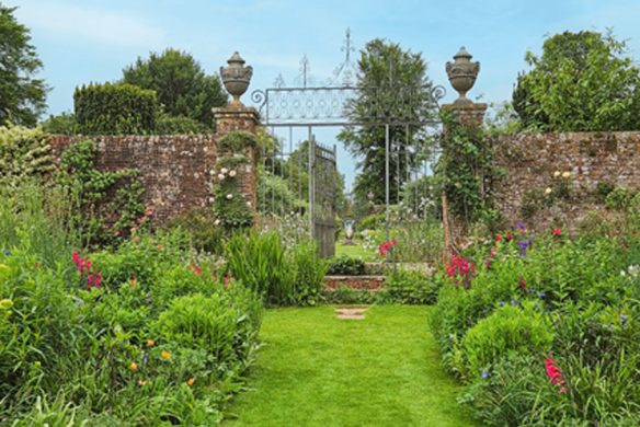 Inspiriert von Gärtnern wie Gott in England aus dem Callwey Verlag: ein üppig grüner Garten mit bunten Blumen, gepflegtem Grasweg und einer Backsteinmauer mit schmiedeeisernem Tor - ideal für die Gartengestaltung nach englischer Gartenkunst.