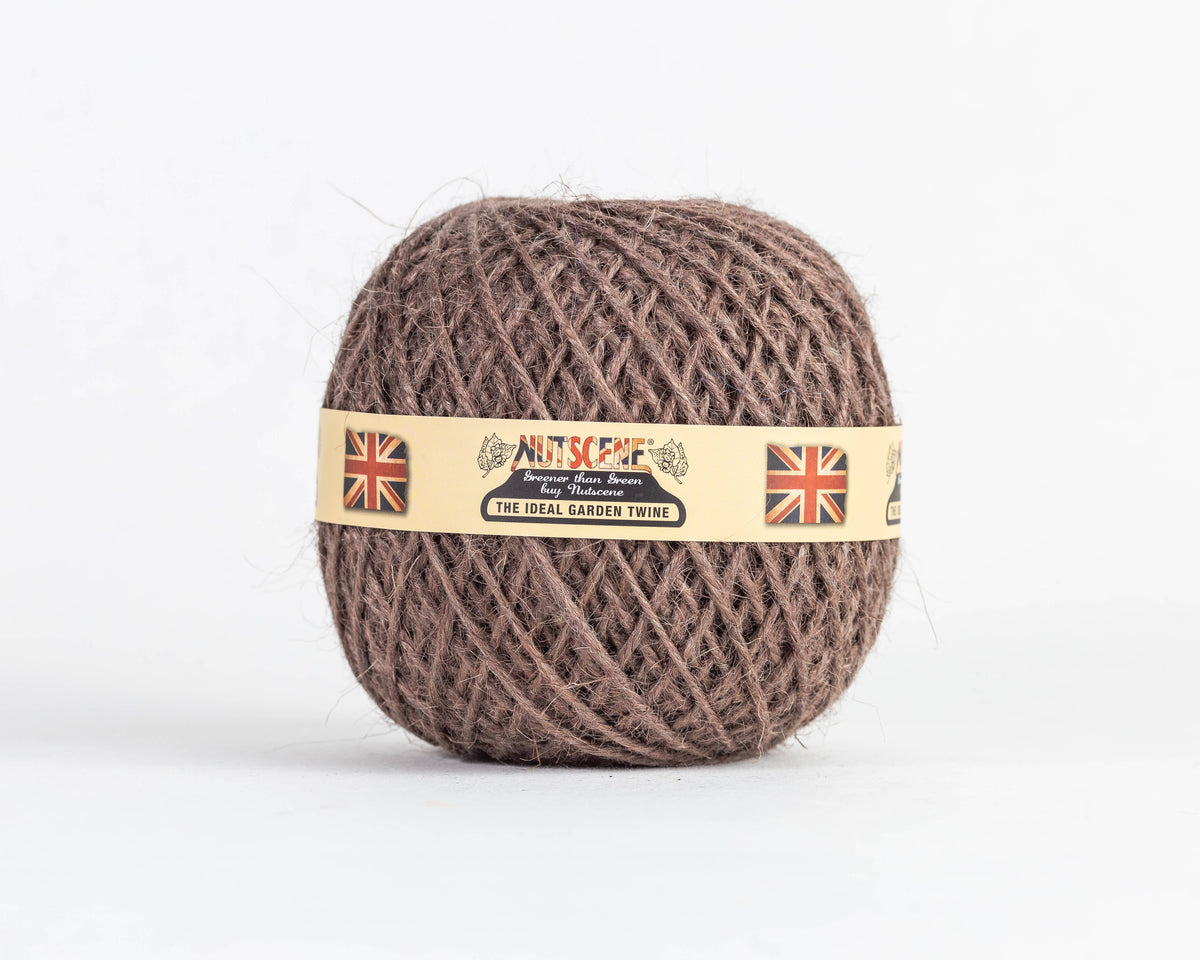 Ein Knäuel „Nutscene | Heritage Jutegarn“ in Braun, 130 m, von Nutscene Twines Ltd, mit einem beigen Etikett, auf dem zwei Union-Jack-Flaggen und der Text „Nutscene – The Ideal Garden Twine“ zu sehen sind. Diese vielseitige Gartenschnur ist vor einem schlichten weißen Hintergrund abgebildet.