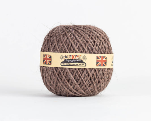 Ein Knäuel „Nutscene | Heritage Jutegarn“ in Braun, 130 m, von Nutscene Twines Ltd, mit einem beigen Etikett, auf dem zwei Union-Jack-Flaggen und der Text „Nutscene – The Ideal Garden Twine“ zu sehen sind. Diese vielseitige Gartenschnur ist vor einem schlichten weißen Hintergrund abgebildet.
