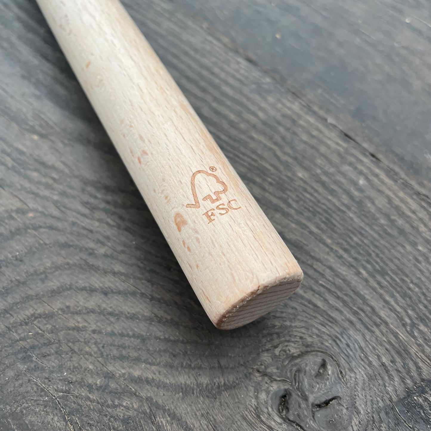 Eine Nahaufnahme des Holzgriffs der Niwaki-Gartenschere aus FSC-zertifiziertem Holz mit eingraviertem FSC-Logo an einem Ende, der auf einer dunklen Holzoberfläche ruht.