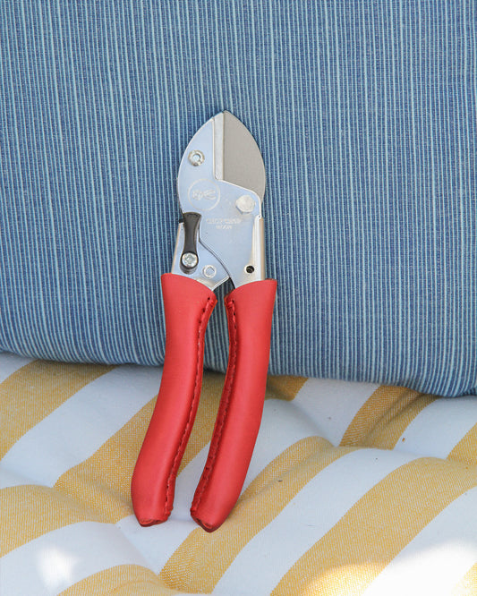 Die Chop Chop Bloom 'Chili Pepper' Exklusive Gartenschere mit roten Griffen steht auf einem blau-weiß gestreiften Kissen, das auf einer gelb-weiß gestreiften Fläche liegt.
