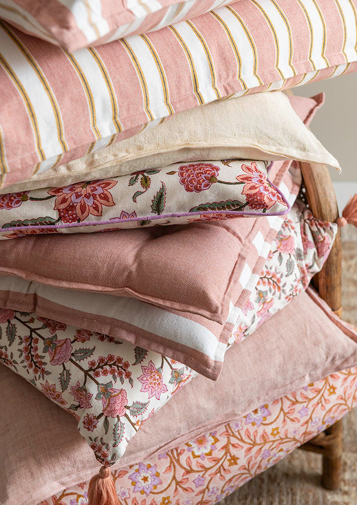 Ein Stapel Bungalow 'Milan Rose' Sitzkissen 45 x 45 cm in Rosa, Creme und Weiß mit Blumen-, Streifen- und Unimustern liegt ordentlich auf einem Holzstuhl.