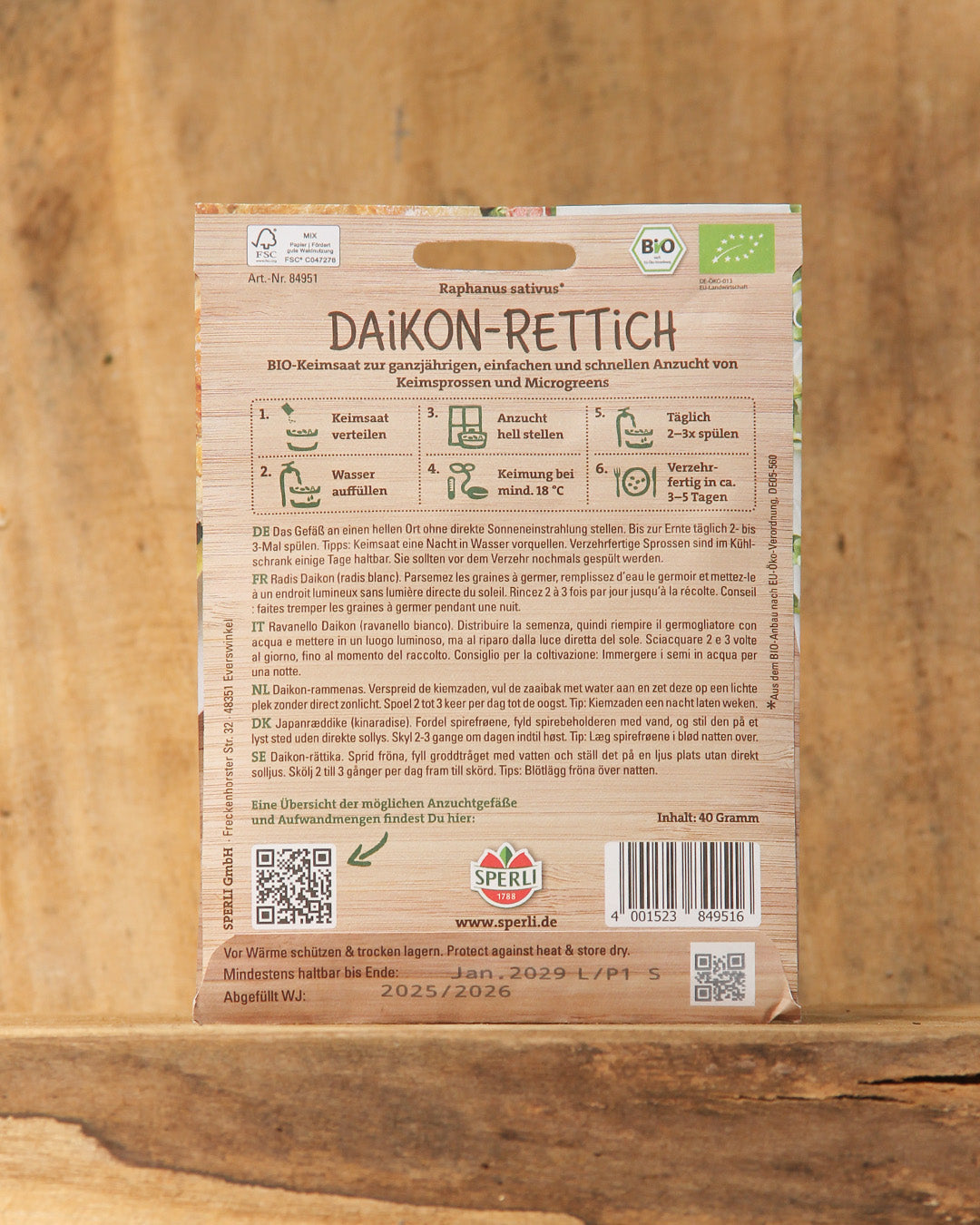 Ein Päckchen Sperli's | Bio Keimsprossen Saatgut 'Daikon-Rettich' steht aufrecht auf einer Holzunterlage, darauf ein deutscher Text mit Pflanzanleitung und Produktdetails.