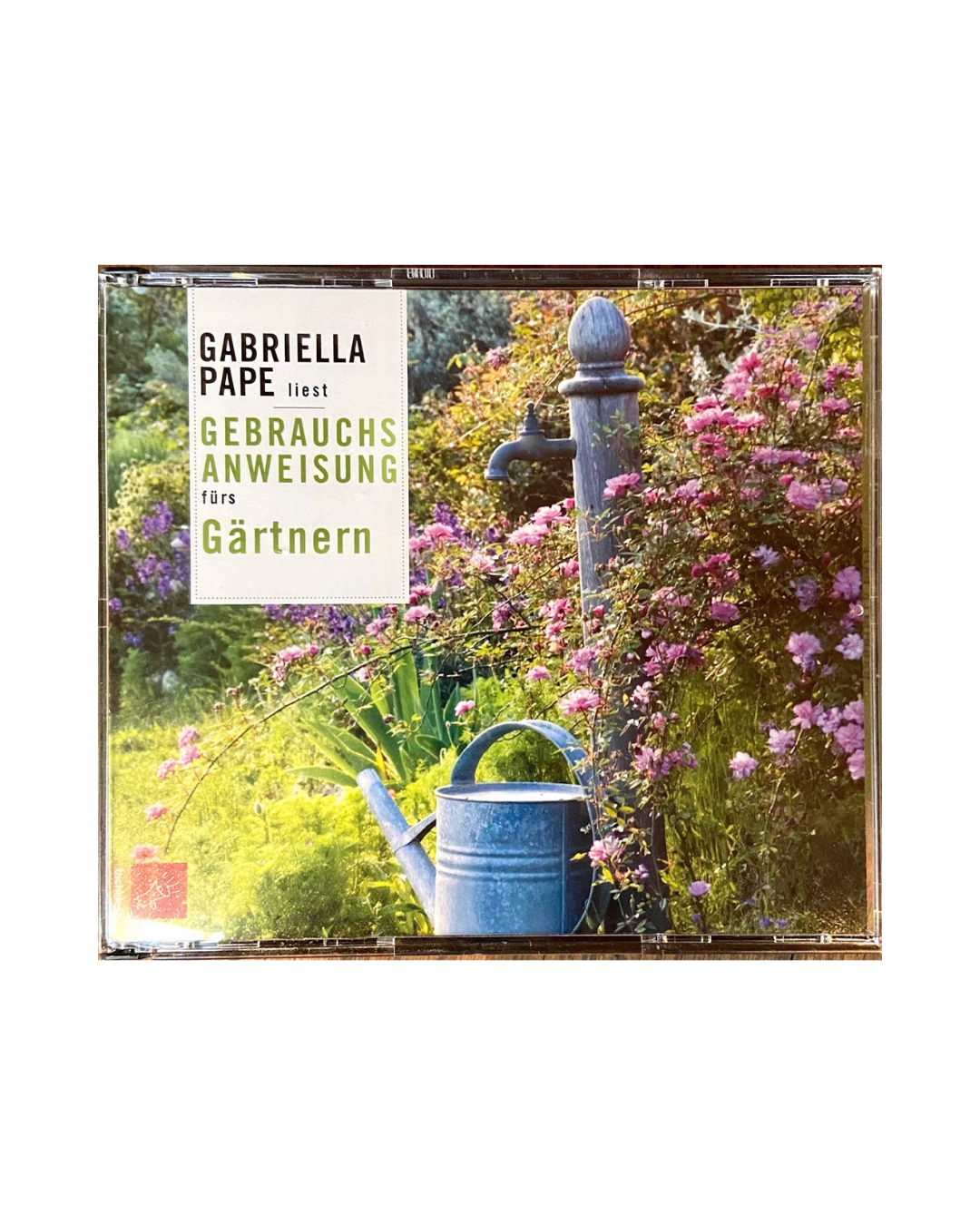 Das Cover des Hörbuchs Gebrauchsanweisung fürs Gärtnern | Praxis & Tipps Hörbuch von Gabriella Pape zeigt einen üppigen Garten mit rosa Blumen, einer rustikalen Wasserpumpe und einer metallenen Gießkanne. Der Text lautet: Gabriella Pape liest Gebrauchsanweisung fürs Gärtnern.