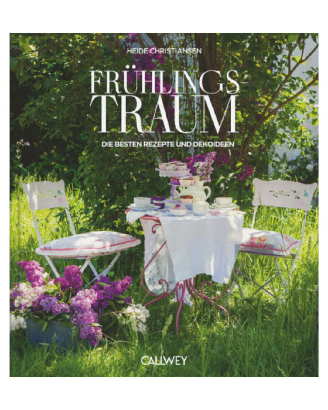 Ein kleiner Tisch mit weißem Tuch, Teetassen, Kuchen und Osterdeko steht zwischen zwei weißen Stühlen inmitten blühenden Flieders. In dem üppigen Garten liegt das Buch "Frühlingstraum | Rezepte für Frühlingsgefühle und österliche Anlässe" vom Callwey Verlag aus.